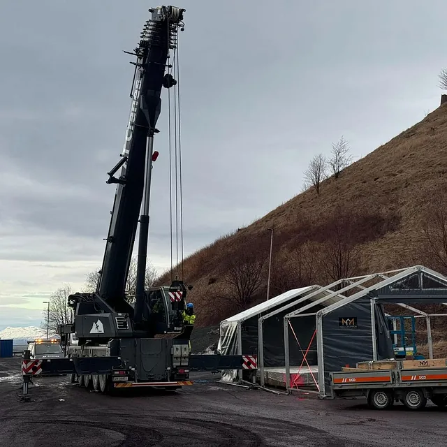 Mobilkran løfter elementer ved oppføring av teltbygg nær skråning.