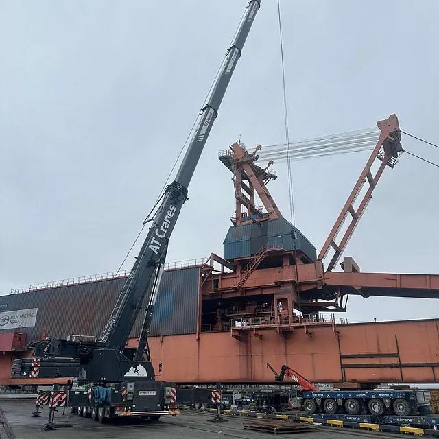 Stor mobilkran fra AT Cranes løfter ved industriområde med lasteanlegg.