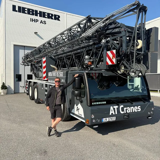 Mann står foran stor mobilkran fra AT Cranes utenfor verksted.