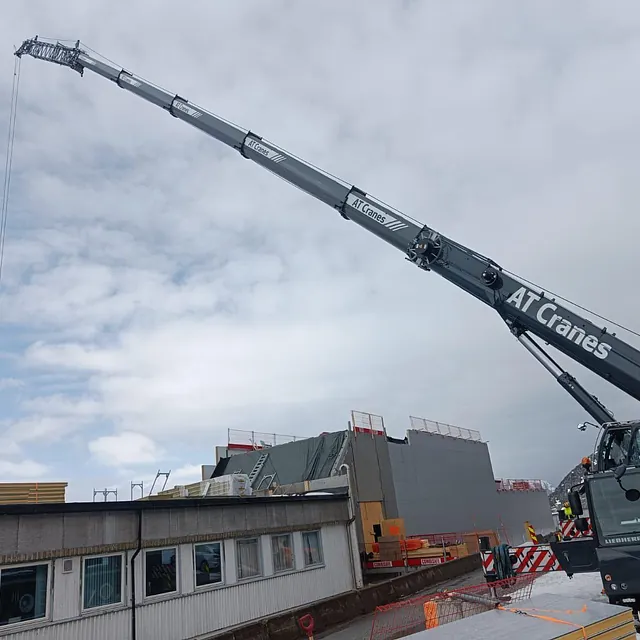 Mobilkran med lang bom løfter materialer ved takarbeid på bygg.